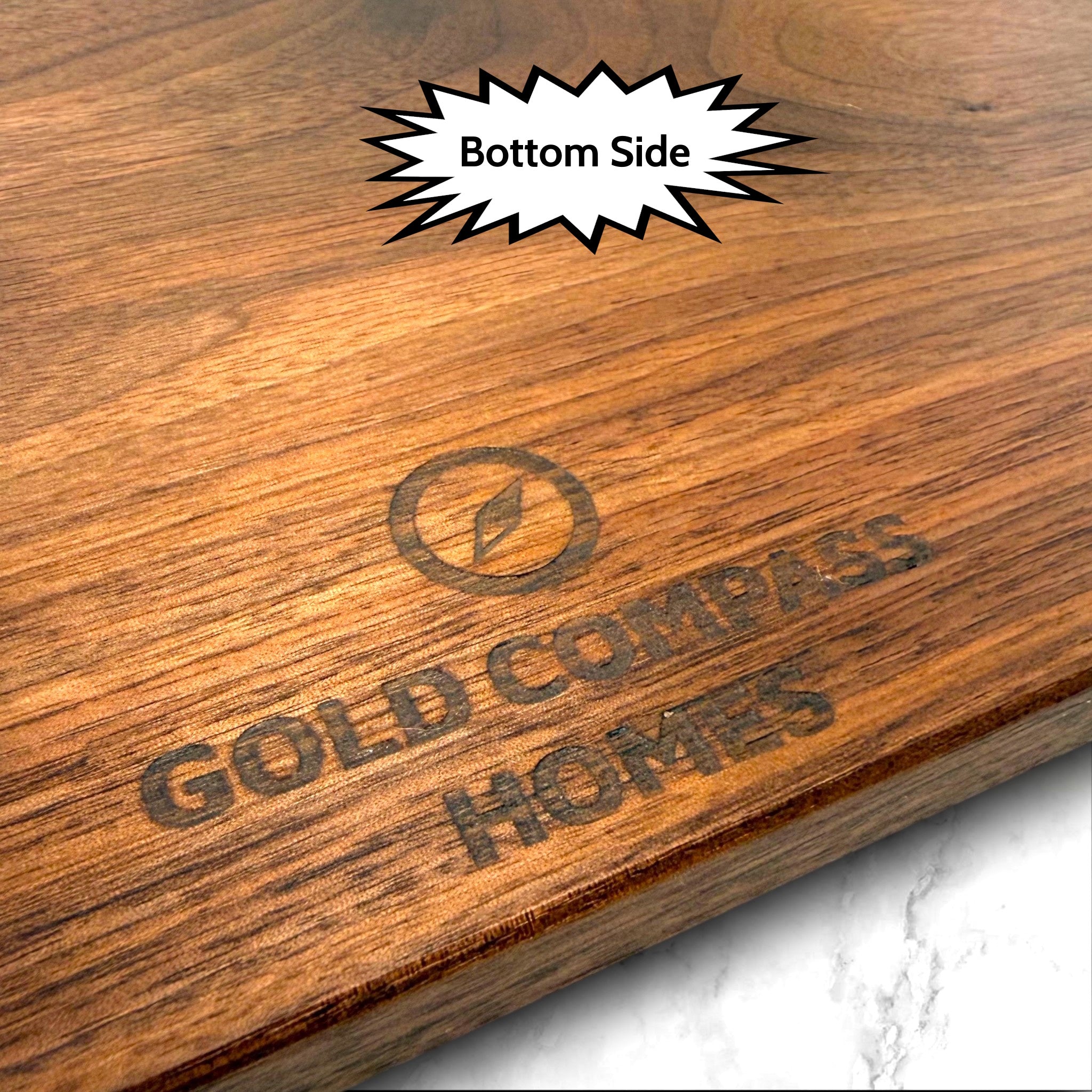 Black walnut cutting board with 'Gold Compass Homes' branding on a marble background