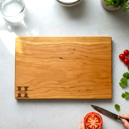 Cherry wooden cutting board with personalized engraving on a kitchen counter.