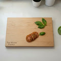 Maple wooden cutting board with personalized laser engraved design and text on a white kitchen countertop.