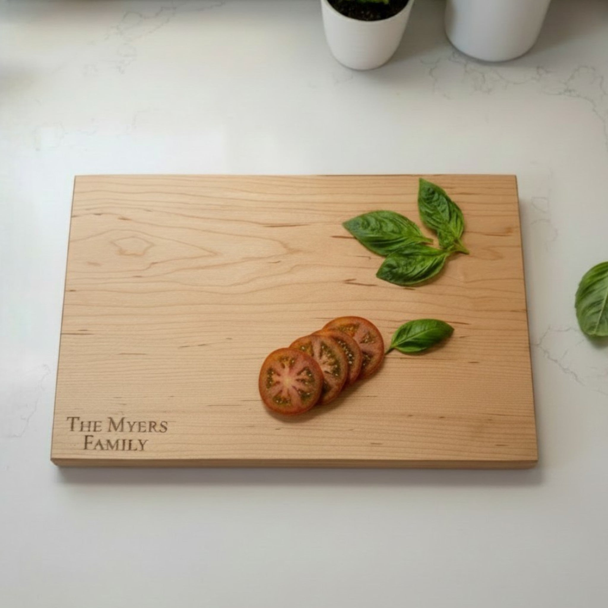 Maple wooden cutting board with personalized laser engraved design and text on a white kitchen countertop.