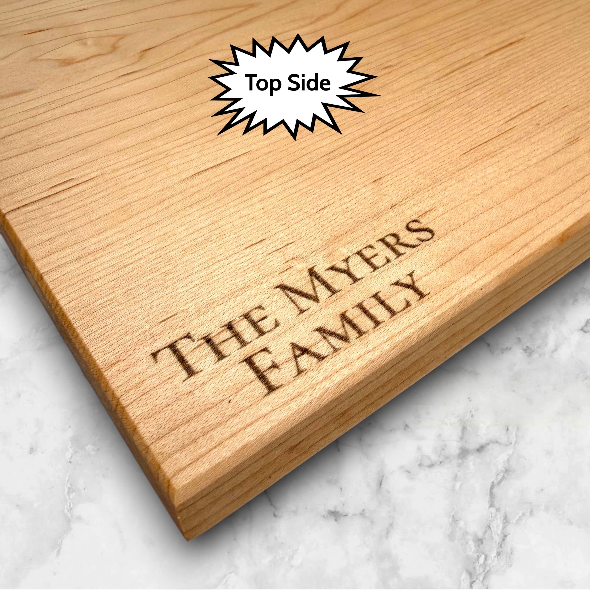 Maple wooden cutting board with personalized laser engraved design and text on a white kitchen countertop.