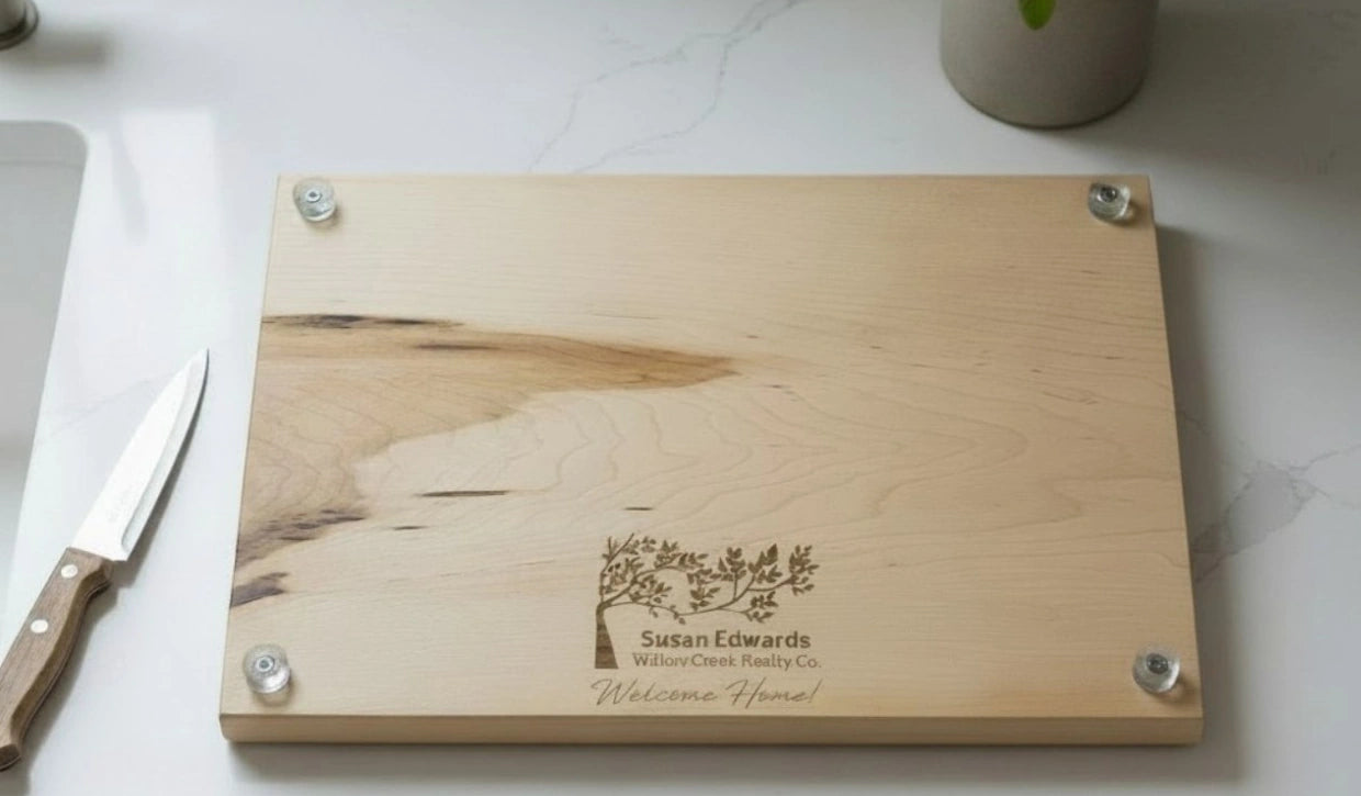 Maple wooden cutting board with personalized laser engraved design and text on a white kitchen countertop.